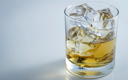 Стакан виски со льдом на светлом фоне &mdash; янтарный напиток с кубиками льда